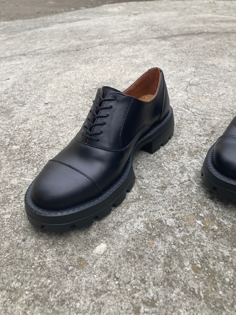 May include: Black leather lace-up shoes with a chunky rubber sole. The shoes have a cap toe design and a slightly rounded toe.