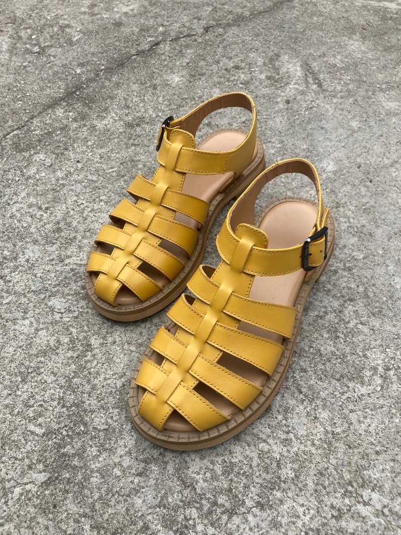 May include: A pair of yellow leather sandals with a caged design and a buckle closure. The sandals have a thick, flat sole.