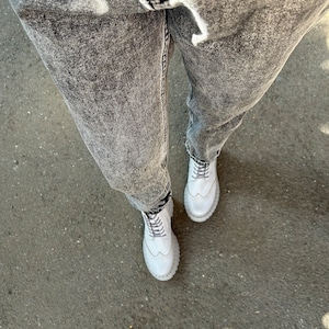 May include: A pair of white leather lace-up boots with a chunky sole. The boots are worn with gray acid wash jeans.