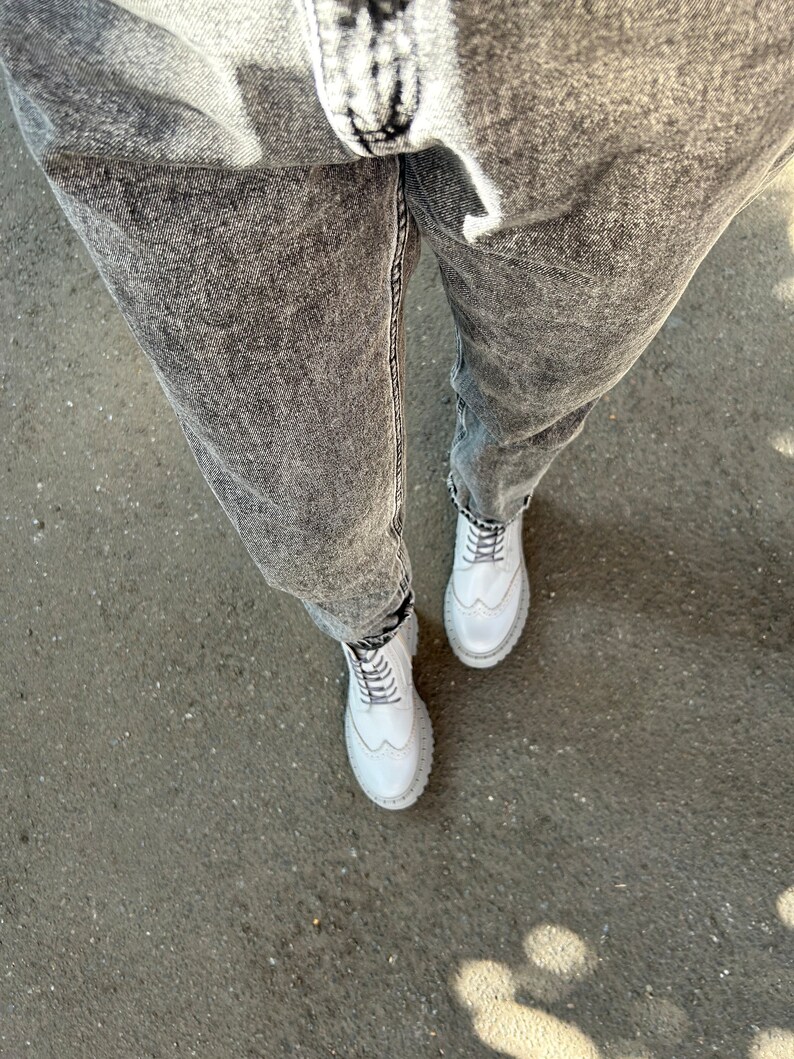 May include: A pair of white leather lace-up boots with a chunky sole. The boots are worn with gray acid wash jeans.