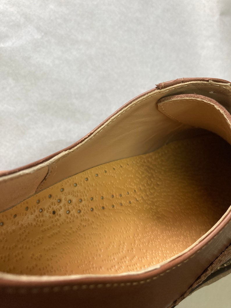 May include: Close-up of the inside of a brown leather shoe. The insole is a light brown color and has a textured pattern of small dots.