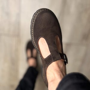 Puede incluir: Zapatos T-bar de ante marr&oacute;n con cierre de hebilla. Los zapatos tienen una puntera redondeada y una suela gruesa cosida. El dise&ntilde;o T-bar presenta una correa que se extiende desde la pala hasta el tobillo. C&oacute;modos y elegantes.