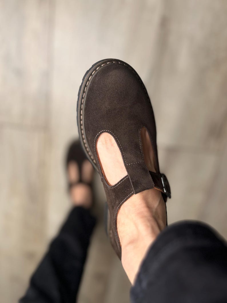 Puede incluir: Zapatos T-bar de ante marr&oacute;n con cierre de hebilla. Los zapatos tienen una puntera redondeada y una suela gruesa cosida. El dise&ntilde;o T-bar presenta una correa que se extiende desde la pala hasta el tobillo. C&oacute;modos y elegantes.