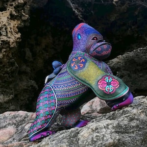 May include: A colorful, intricately patterned wooden gorilla sculpture with a green, blue, and yellow design. The gorilla is standing on a rocky surface.