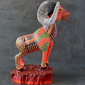 May include: A colorful wooden sculpture of a ram with large horns. The ram is painted in shades of red, orange, yellow, green, and black. The sculpture is standing on a wooden base.