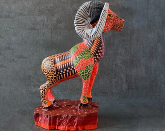 May include: A colorful wooden sculpture of a ram with large horns. The ram is painted in shades of red, orange, yellow, green, and black. The sculpture is standing on a wooden base.