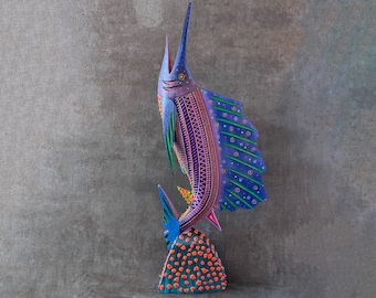 May include: A colorful wooden sculpture of a marlin fish with purple, blue, green, and pink paint. The fish is standing on a base with orange and blue paint.
