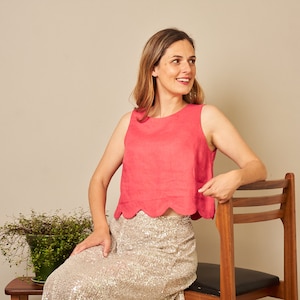 May include: A sleeveless, bright pink cropped top featuring a rounded scalloped hemline. The top is paired with a long, shimmering gold sequined skirt that reaches down to the floor, creating a distinct contrast in texture and color.