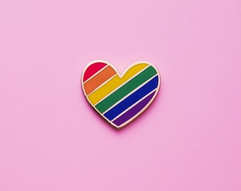 May include: A rainbow heart-shaped pin with a gold outline. The heart is filled with the colors of the rainbow, starting with red at the top and ending with purple at the bottom.