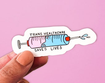 Può includere: Un adesivo raffigurante una siringa a fumetti, metà rosa e metà blu, con la scritta "TRANS HEALTHCARE SAVES LIVES". La siringa ha uno stantuffo rosso ed è ambientata su uno sfondo rosa.