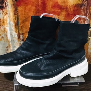 Könnte beinhalten: Ein Paar schwarze Stiefeletten mit einer weißen Plateau-Sohle. Die Stiefeletten haben einen Reißverschluss an der Seite und eine leicht schlabberige Passform.