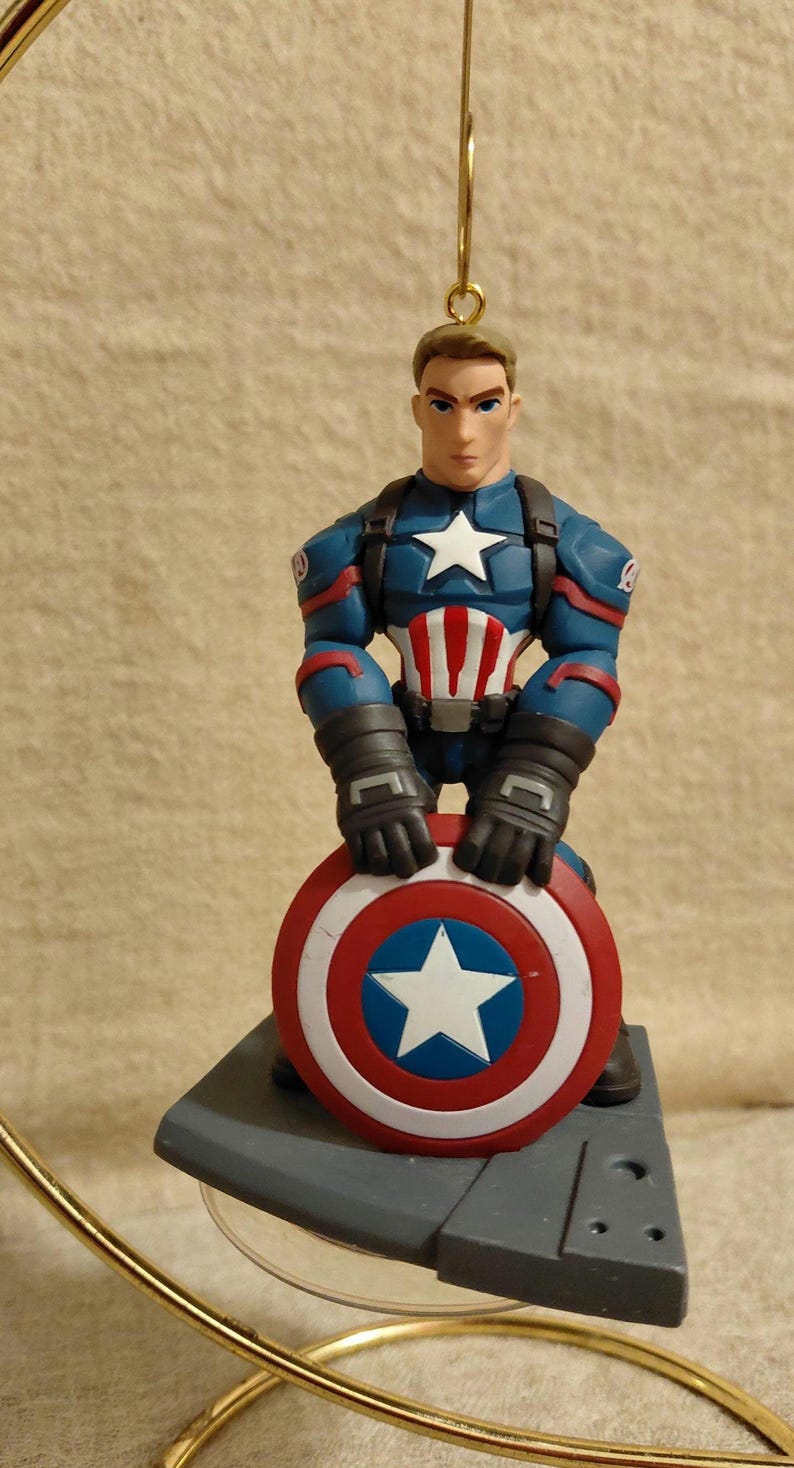 Puede incluir: Figura de Capit&aacute;n Am&eacute;rica, con el personaje en uniforme azul y rojo, sosteniendo su escudo. El escudo es rojo, blanco y azul con una estrella blanca. Es un art&iacute;culo de colecci&oacute;n.