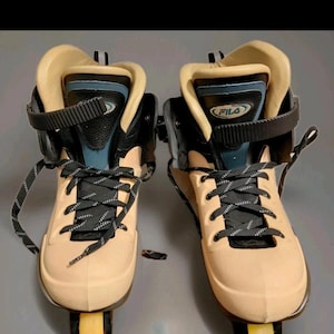 May include: Pair of beige and black inline skates with black laces and yellow wheels. The skates have a high-top design with a padded collar and the brand name "FILA" visible on the tongue.
