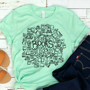 Puede incluir: Una camiseta verde menta con un gráfico negro de libros y el texto "Books" repetido varias veces. La camiseta se combina con unos vaqueros azul oscuro.