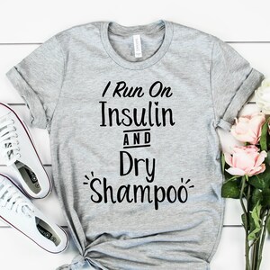 Puede incluir: Camiseta gris con el texto "I Run On Insulin And Dry Shampoo" impreso en negro.