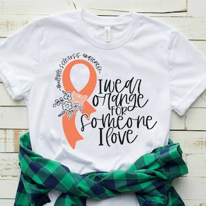 May include: White t-shirt with an orange ribbon, flowers, and butterflies. The text reads "I wear orange for someone I love - Multiple Sclerosis Awareness"