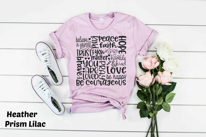 May include: A heather prism lilac t-shirt with a black graphic print of words including "believe", "peace", "faith", "hope", "trust", "you", "matter", "humble", "brave", "pray", "love", "be courageous", and "be happy".