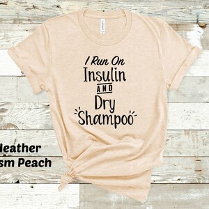 Puede incluir: Una camiseta beige con el texto "I Run On Insulin And Dry Shampoo" impreso en negro.