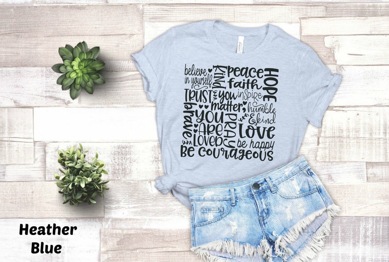 May include: A light blue t-shirt with a black word art design that reads "Believe in yourself, Peace, Faith, Trust you, Inspire, Matter, Humble, You are loved, Be happy, Be courageous".