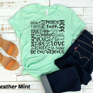 May include: A heather mint green t-shirt with a black graphic print of the words "believe in yourself", "peace", "faith", "hope", "trust", "you inspire", "matter", "humble", "you", "pray", "are", "love", "love", "be happy", "be courageous".