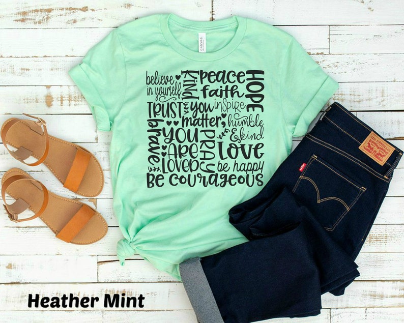 May include: A heather mint green t-shirt with a black graphic print of the words "believe in yourself", "peace", "faith", "hope", "trust", "you inspire", "matter", "humble", "you", "pray", "are", "love", "love", "be happy", "be courageous".
