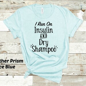 Puede incluir: Una camiseta azul claro con el texto "I Run On Insulin And Dry Shampoo" impreso en negro.