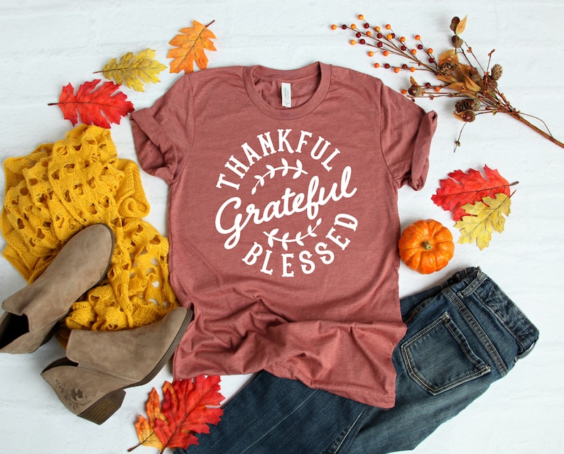 Może przedstawiać: Koszulka w kolorze bordowym z napisem "Thankful Grateful Blessed" w białym k&oacute;łku z wzorem liści.