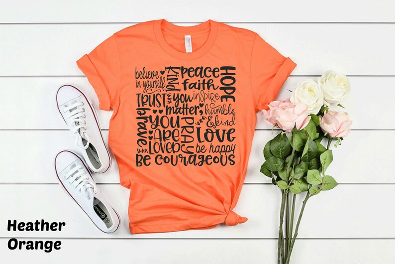 May include: Orange t-shirt with a black graphic print of words like "believe", "peace", "hope", "trust", "love", and "be courageous".
