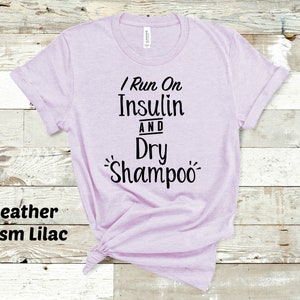 Puede incluir: Una camiseta de color lila prisma heather con el texto "I Run On Insulin And Dry Shampoo" impreso en negro.