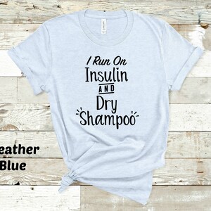 Puede incluir: Una camiseta azul claro con el texto "I Run On Insulin And Dry Shampoo" impreso en negro.