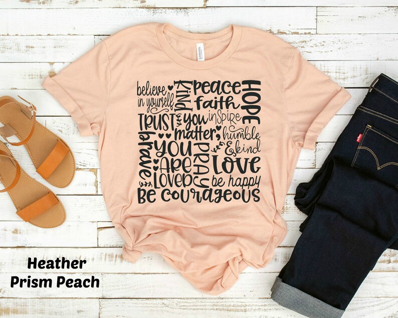 May include: A peach-colored t-shirt with a black graphic design featuring the words "believe", "peace", "hope", "trust", "you", "matter", "love", "be courageous", and more. The shirt is made of a soft, comfortable material.