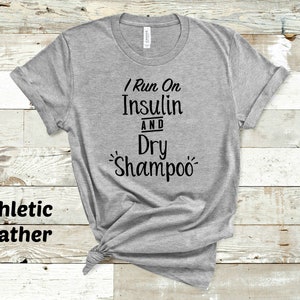 Puede incluir: Camiseta gris con el texto "I Run On Insulin And Dry Shampoo" impreso en negro.
