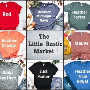 Może przedstawiać: Dziewięć r&oacute;żnych kolorowych koszulek z r&oacute;żnymi nadrukowanymi tekstami. Tekst zawiera "Red", "Heather Midnight Navy", "Heather Forest", "Heather Orange", "The Little Rustic Market", "Mauve", "Deep Heather", "Black Heather" i "Heather True Royal".