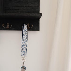 May include: A white and blue floral patterned key chain with a silver key attached to a black wooden hook.