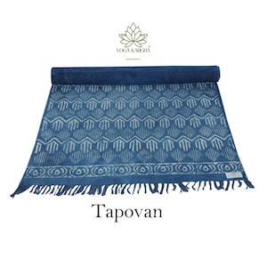 May include: A blue cotton yoga mat with a white geometric pattern and fringe. The mat is rolled up and the brand name "Yoga Karcha" is visible. The text "Tapovan" is printed below the mat.