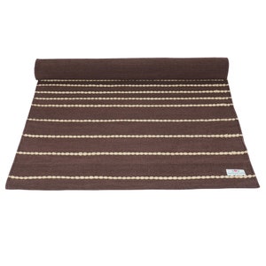 May include: A brown and cream striped rug with a woven texture. The rug is rolled up at the top and has a small label that says "Handmade".