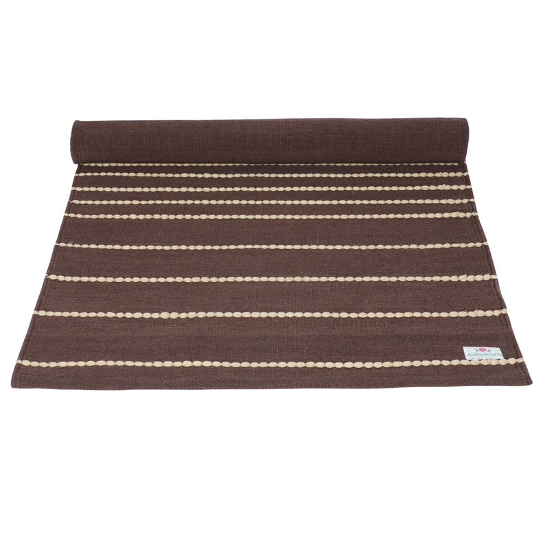 May include: A brown and cream striped rug with a woven texture. The rug is rolled up at the top and has a small label that says "Handmade".