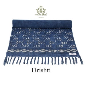 May include: A blue cotton yoga mat with a white leaf pattern and fringe. The mat is rolled up and has a label that says "Yoga Kareha". The text "Dristhi" is printed below the mat.