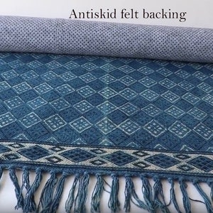 May include: A blue and white patterned rug with fringe on the ends. The rug has an anti-skid felt backing.