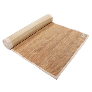 K&ouml;nnte beinhalten: Eine zusammengerollte Yogamatte aus Naturfasern mit wei&szlig;em Rand. Die Matte besteht aus gewebtem Stroh und ist f&uuml;r die Verwendung auf dem Boden konzipiert.