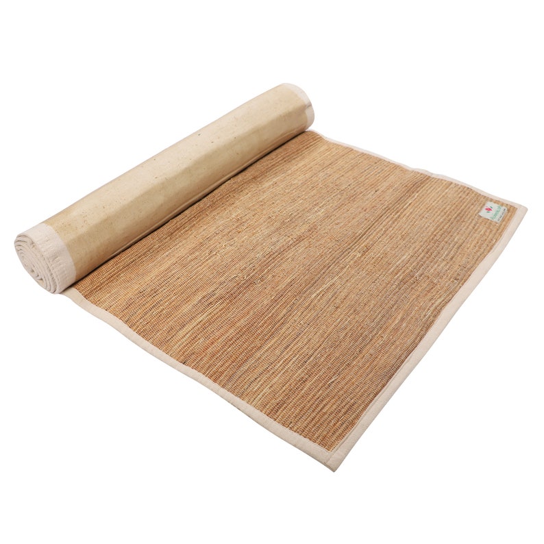 K&ouml;nnte beinhalten: Eine zusammengerollte Yogamatte aus Naturfasern mit wei&szlig;em Rand. Die Matte besteht aus gewebtem Stroh und ist f&uuml;r die Verwendung auf dem Boden konzipiert.