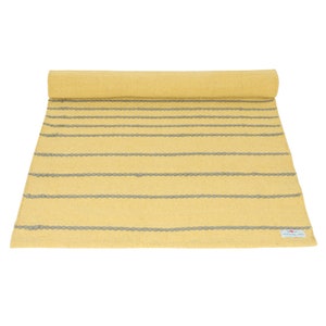 May include: A yellow and gray striped rug with a "Remarkable" label. The rug is rolled up and has a textured surface.