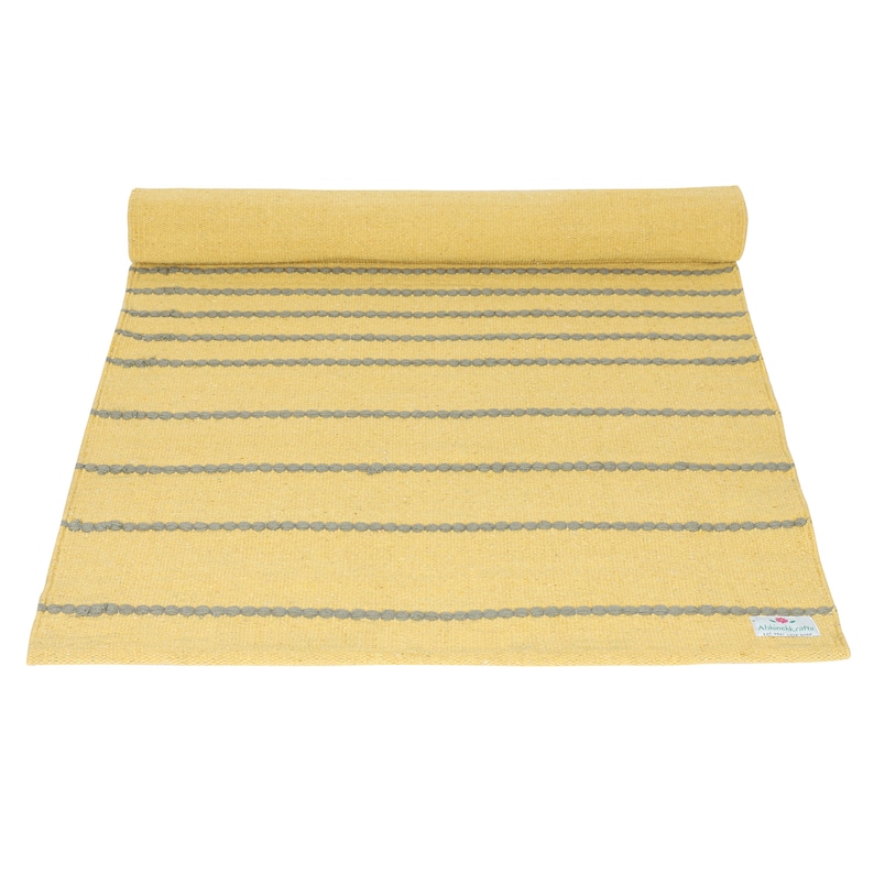 May include: A yellow and gray striped rug with a "Remarkable" label. The rug is rolled up and has a textured surface.