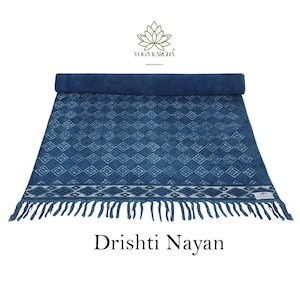 May include: A blue cotton yoga mat with a white diamond pattern and fringe. The mat is rolled up and has a label that says "Yoga Kargha" and "Abode Crafts". The text "Dristhi Nayan" is written below the mat.