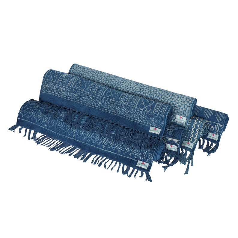 May include: A set of three indigo blue cotton rugs with white geometric patterns. The rugs have fringed edges and are rolled up.