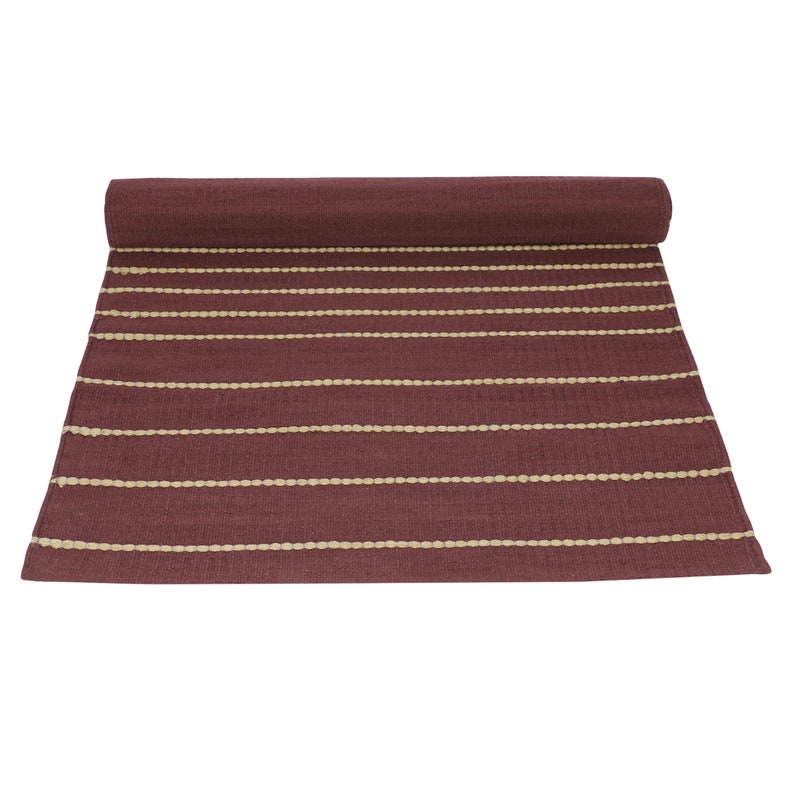 May include: A maroon and cream striped rug with a woven texture. The rug is rolled up and ready to be unfurled.