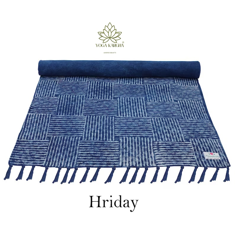 May include: A blue and white striped cotton yoga mat with tassels. The mat is rolled up and has a label that says "Yoga Karigha". The mat is called "Hriday".