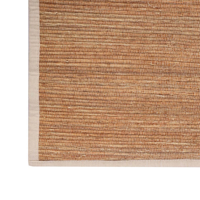 K&ouml;nnte beinhalten: Ein nat&uuml;rlicher gewebter Teppich mit einem beigefarbenen Rand. Der Teppich ist aus Naturfasern gefertigt und hat einen rustikalen Look.