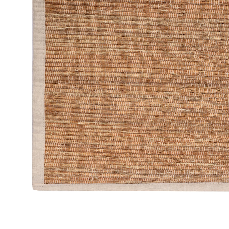 K&ouml;nnte beinhalten: Ein nat&uuml;rlicher gewebter Teppich mit einem beigefarbenen Rand. Der Teppich ist aus Naturfasern gefertigt und hat einen rustikalen Look.