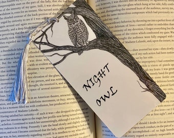 May include: A white bookmark with a black and white illustration of an owl perched on a branch. The bookmark has a black tassel and the text "NIGHT OWL" is written in black cursive.